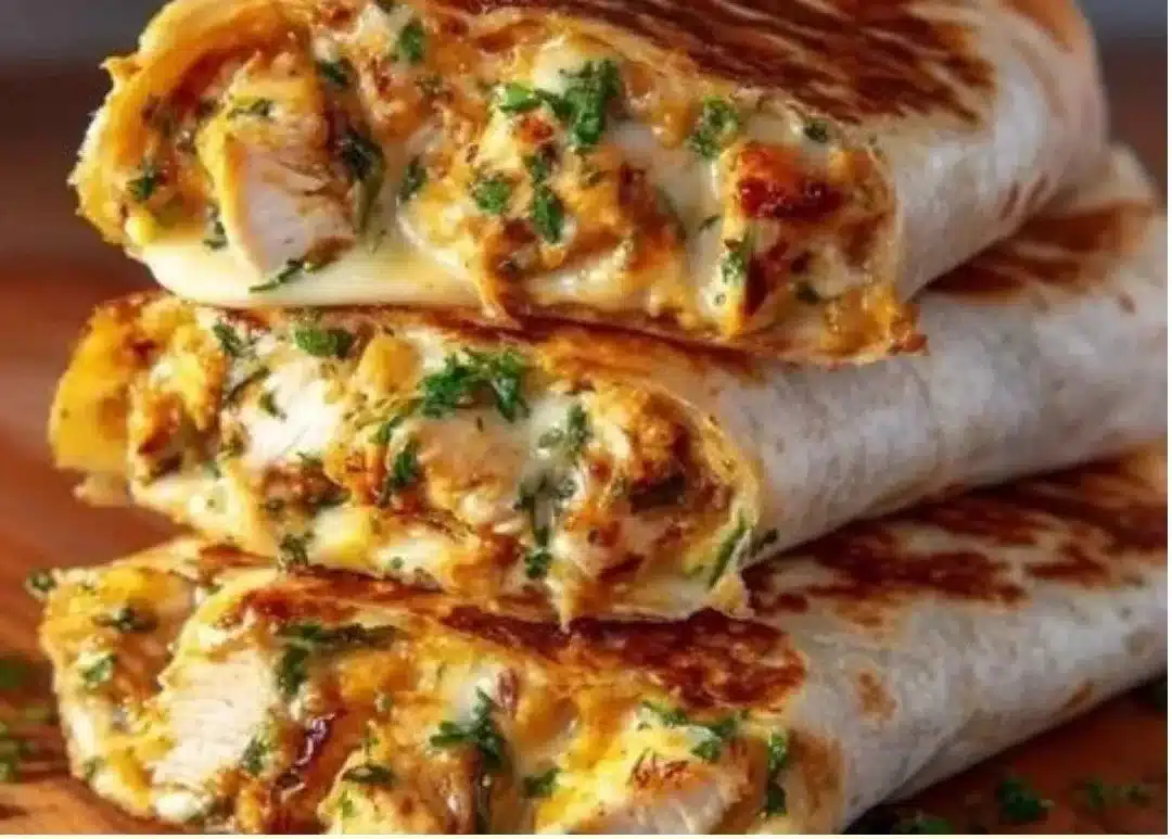 Cheesy garlic chicken wraps on a plate garnished with fresh herbs.
