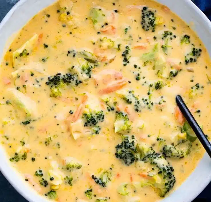 Bowl of homemade broccoli cheddar soup topped with cheese and fresh herbs